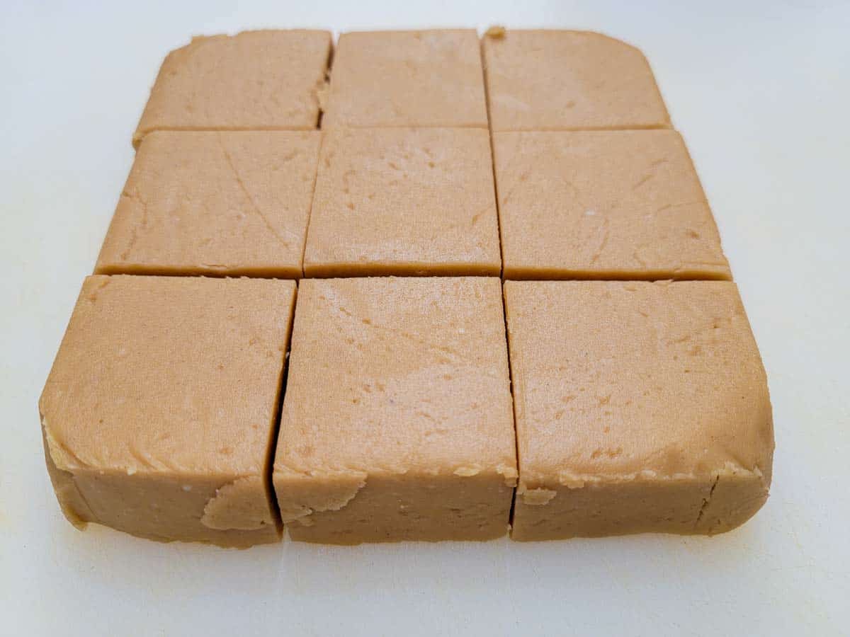a block of fudge cut into 9 pieces on a cutting board.
