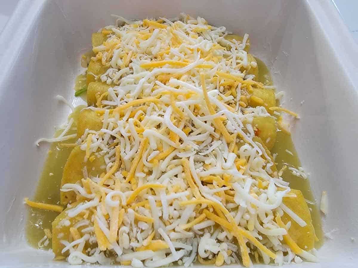 6 corn tortilla shrimp enchiladas topped with green sauce and cheese in a casserole dish.
