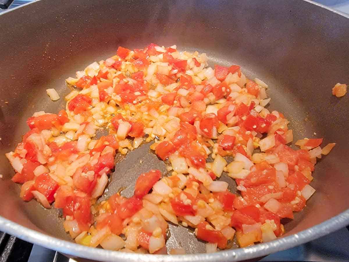 tomatoes, onions, garlic, and cumin cooking in a pan.