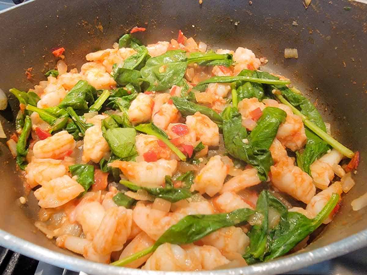 tomatoes, onions, garlic, shrimp, spinach leaves and cumin cooking in a pan.