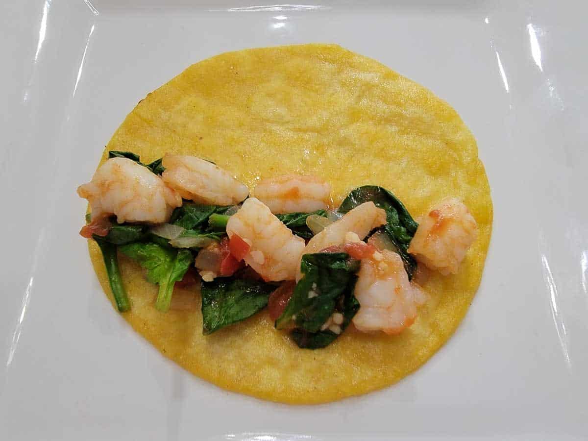 tomatoes, onions, garlic, shrimp, spinach leaves and cumin on a corn tortilla.