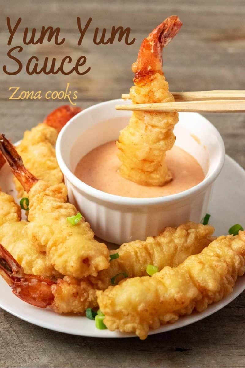a piece of shrimp tempura being dipped into yum yum sauce.