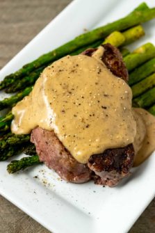 a Filet Mignon topped with Bourbon Sauce over asparagus on a plate.
