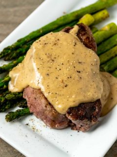 a Filet Mignon topped with Bourbon Sauce over asparagus on a plate.