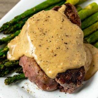 a Filet Mignon topped with Bourbon Sauce over asparagus on a plate.