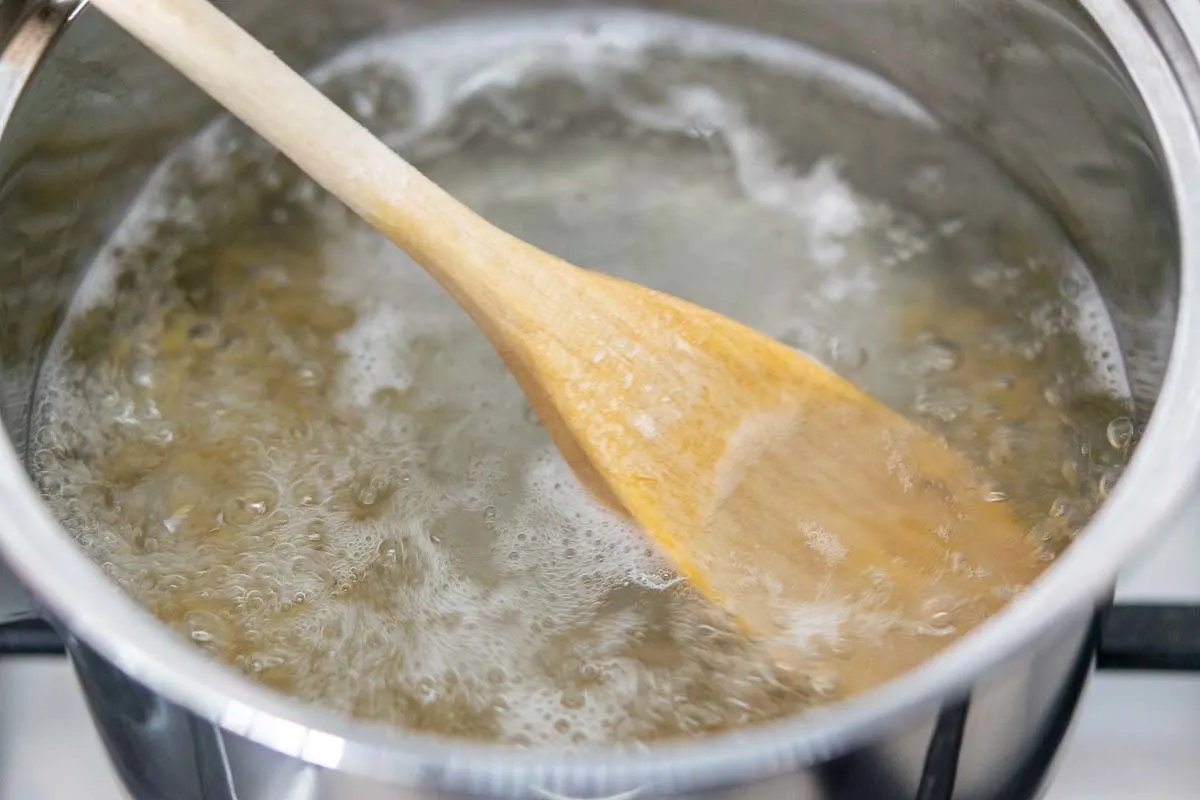 pasta cooking in a pan of boiling water with a wooden spoon resting on the surface of the water.