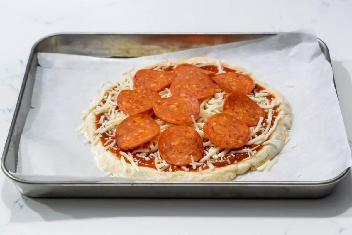 a small uncooked pepperoni pizza on a baking sheet.
