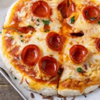 a small pepperoni pizza on a baking sheet.