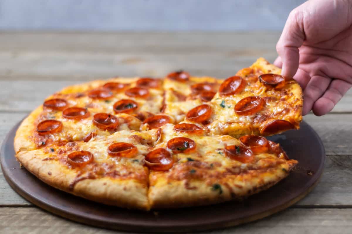 a hand taking a slice of pizza.