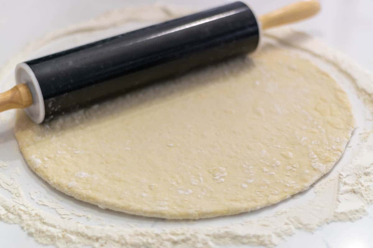 bread maker pizza dough rolled out into a circle with a rolling pin.
