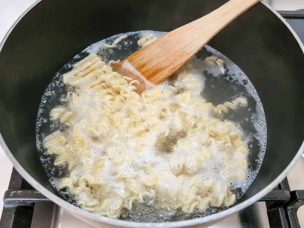a package of ramen noodles boiling in a pan.