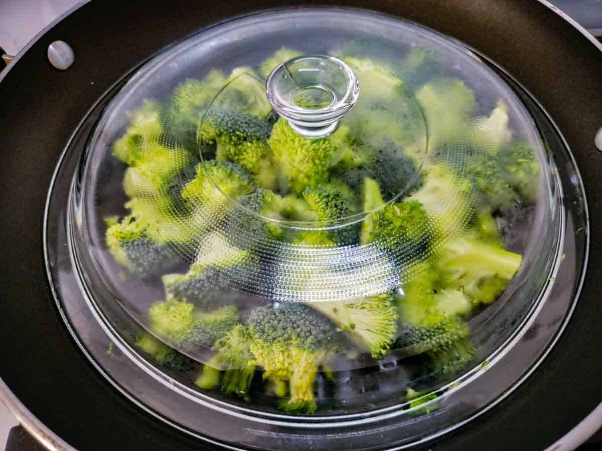 broccoli steaming in a large skillet covered with a lid.