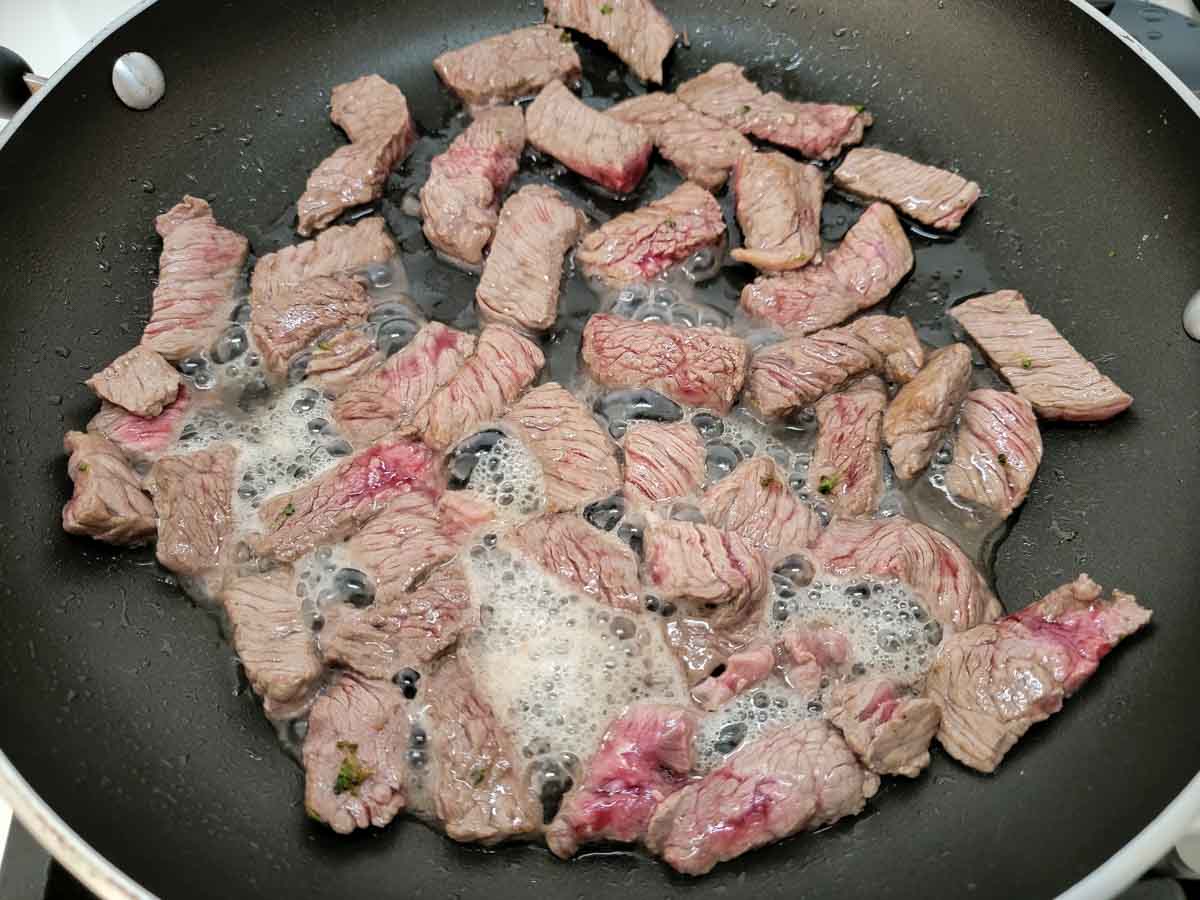 thin sliced sirloin steak cooking in a large skillet.