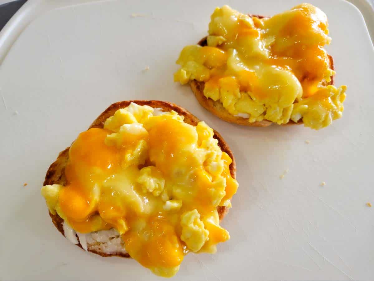 a slice of double cheddar cheese on top of scrambled eggs placed on mayo covered croissant halves.