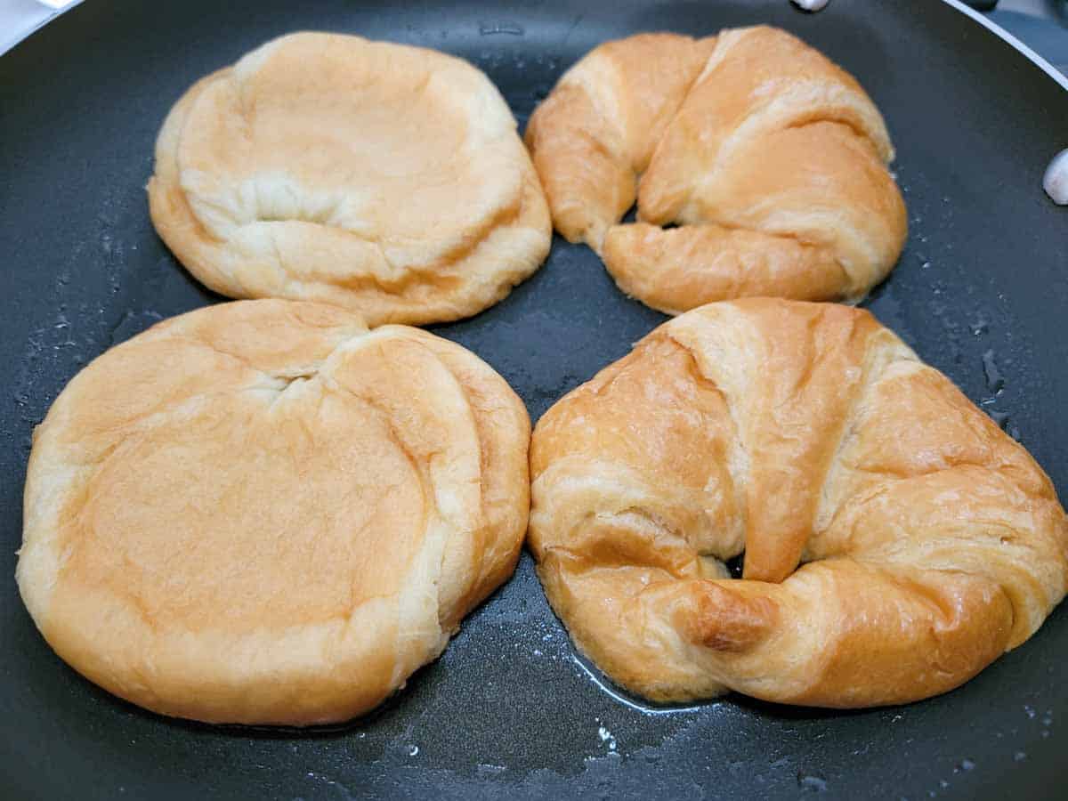 4 halves of croissant frying in a pan.
