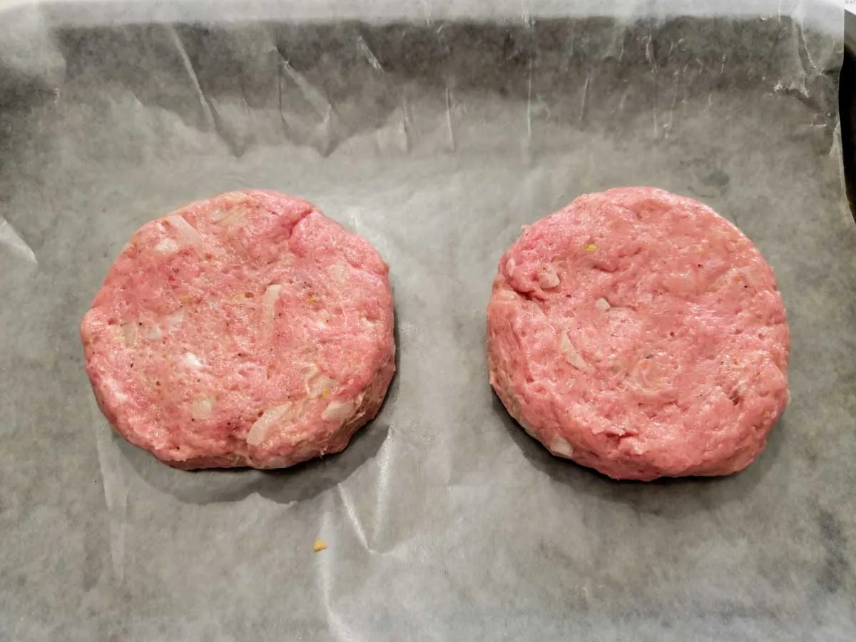 two ground turkey patties on a wax paper.