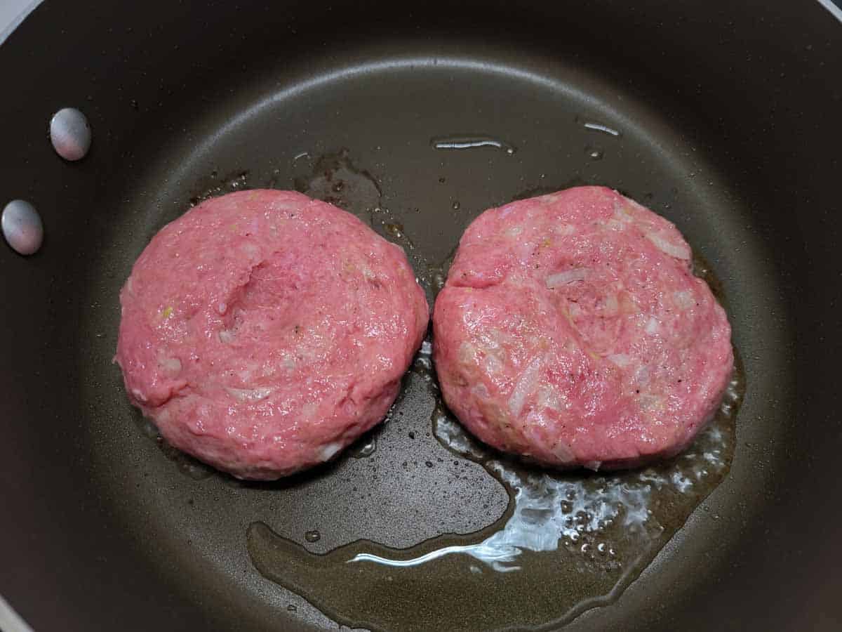 two ground turkey patties frying in a pan.