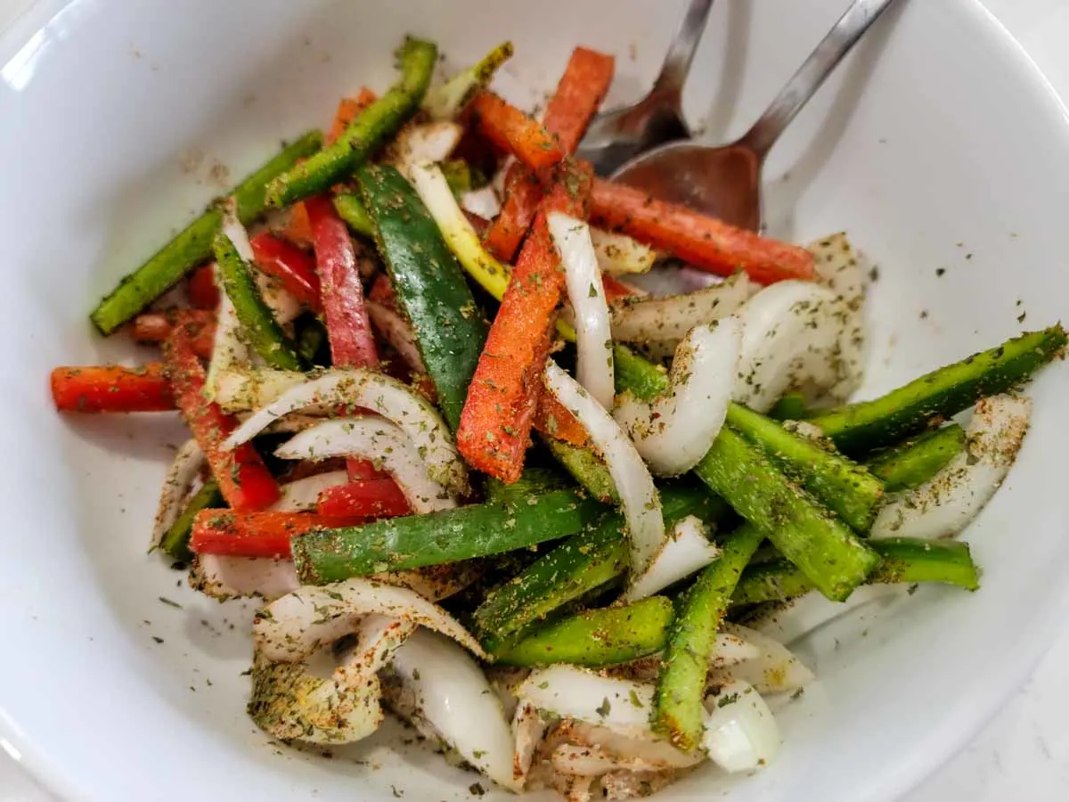 green pepper, red pepper, and onions mixed with fajita seasonings in a bowl.