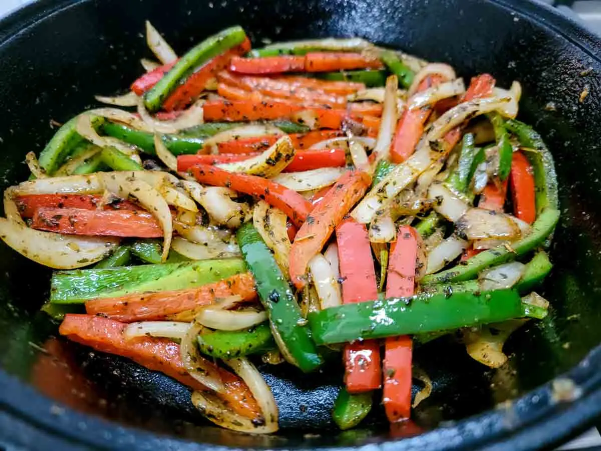 green pepper, red pepper, and onions mixed with fajita seasonings in a cast iron skillet.