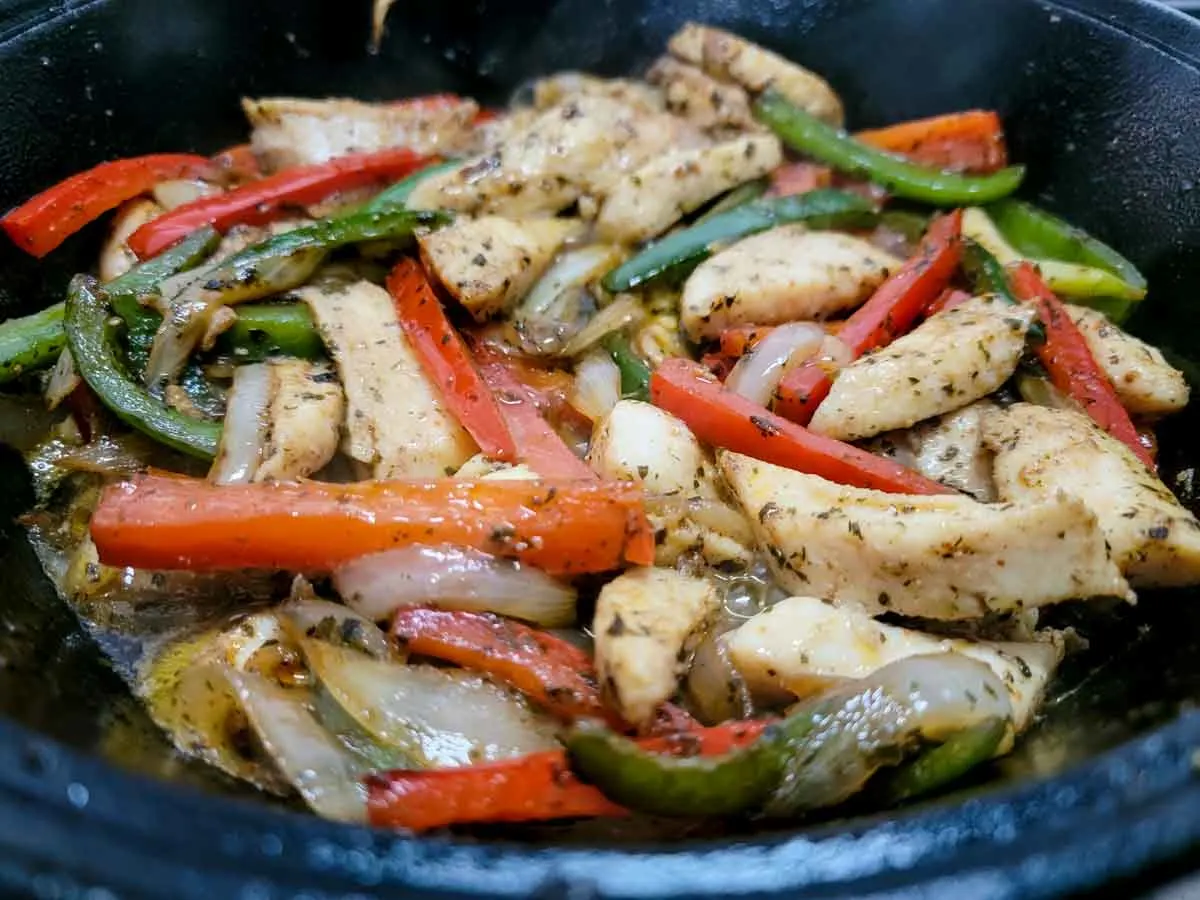 chicken, green pepper, red pepper, and onions mixed with fajita seasonings cooking in a cast iron skillet.