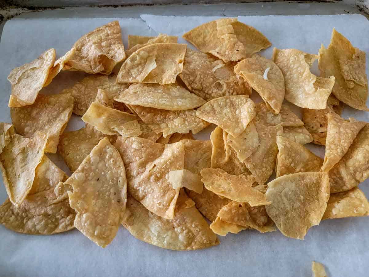 restaurant style tortilla chips spread out on a baking sheet.