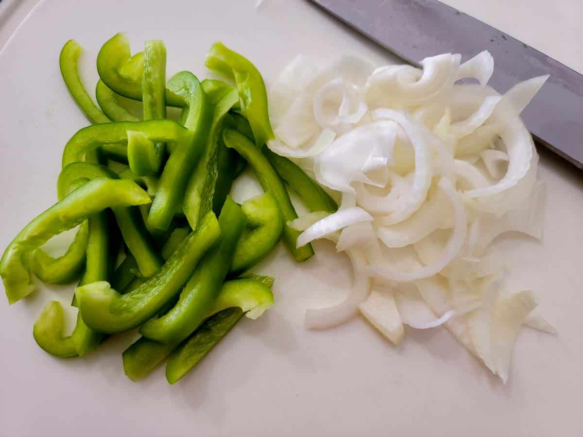 green bell pepper and onion sliced on a cutting board.
