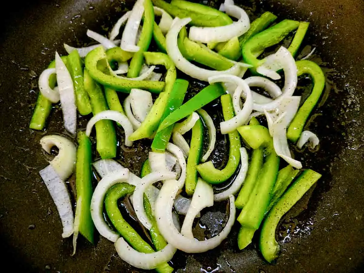 sliced green pepper and onions cooking in a skillet.