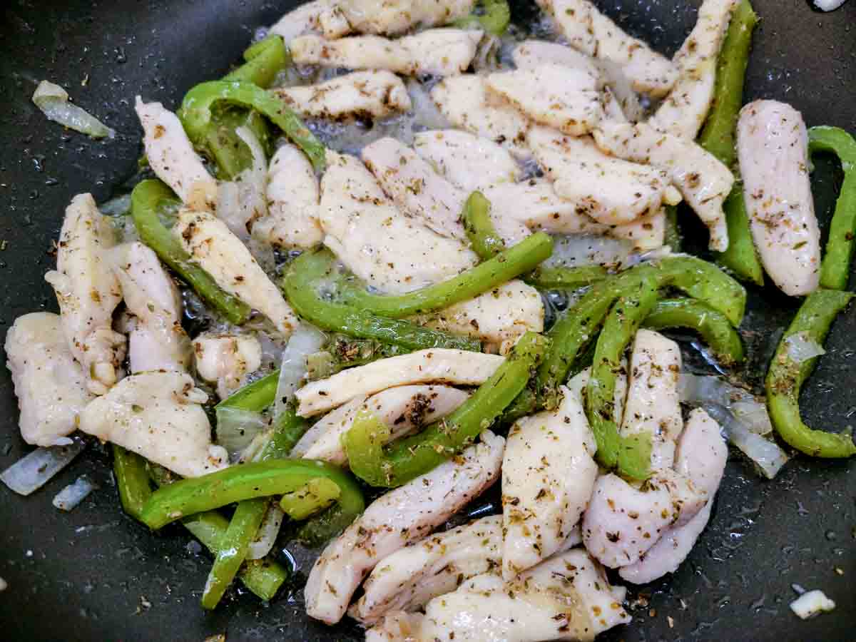 chicken, sliced green pepper and onions cooking in a skillet.