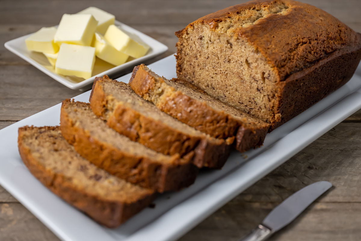 a loaf of banana bread half sliced and a side of butter pats.