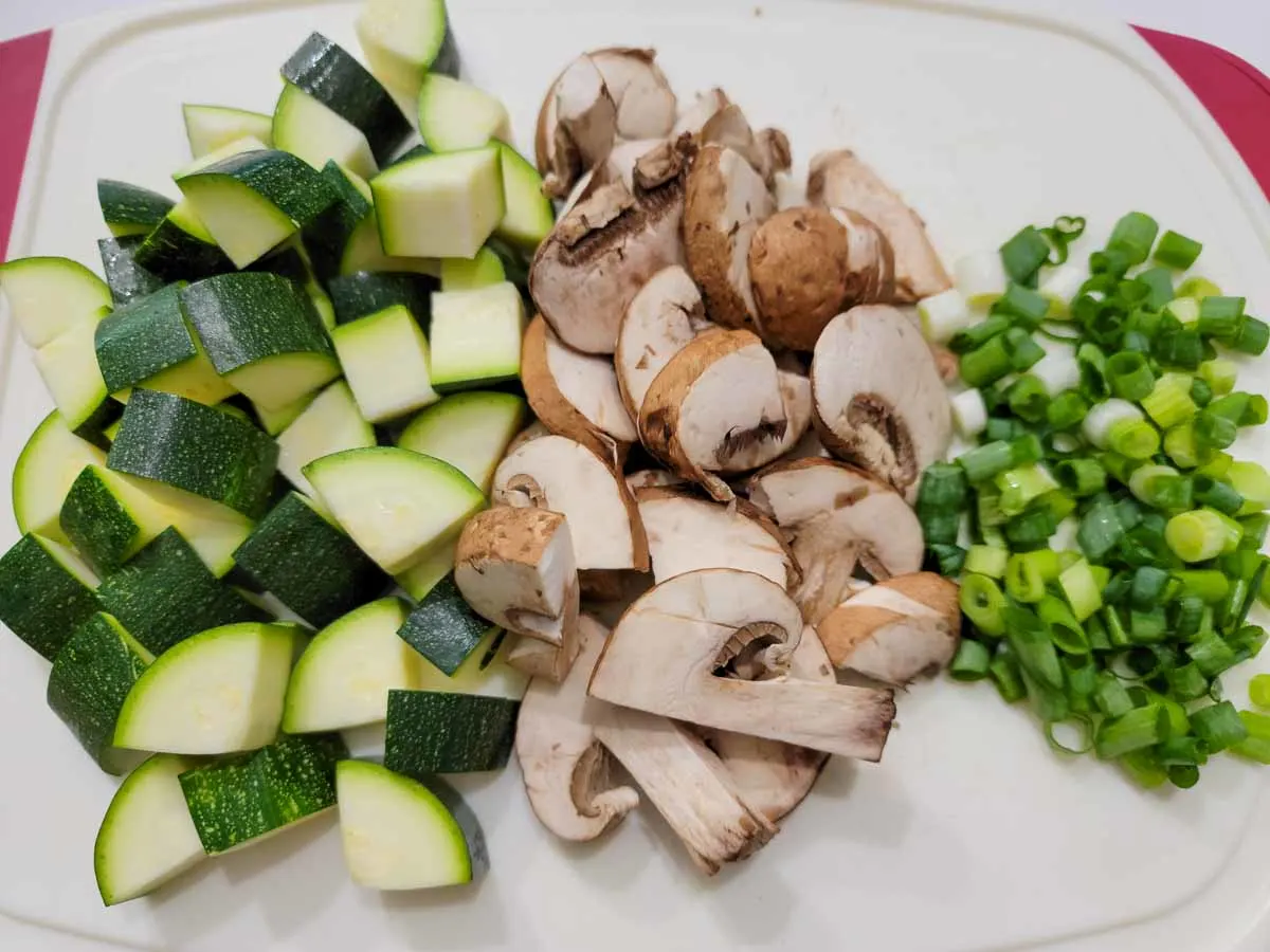 diced zucchini, mushrooms, and green onions on a cutting board.