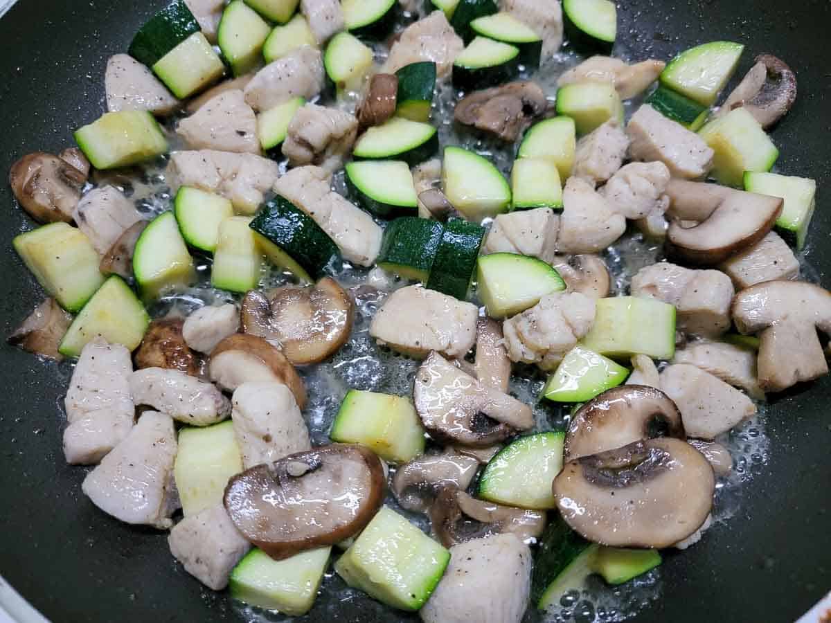 chicken, zucchini, and mushrooms cooking in a skillet.