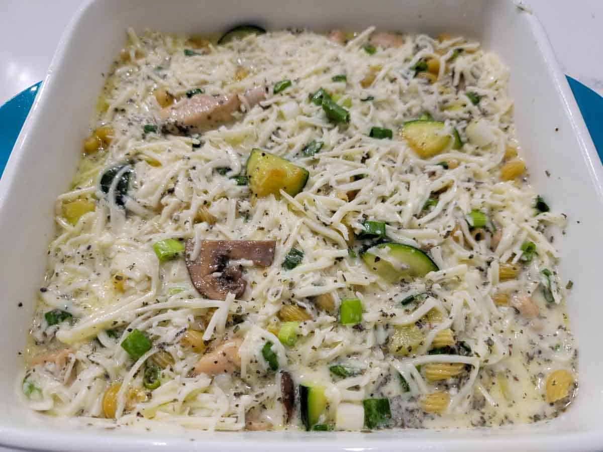cheese sauce mixture layered over chicken and pasta mixture in a casserole dish.