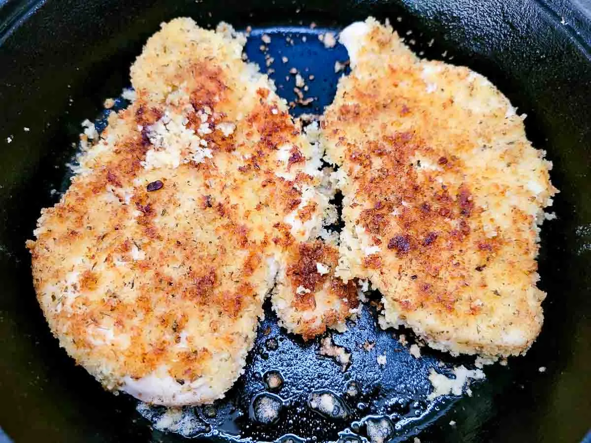 breaded chicken breasts cooking in a skillet.