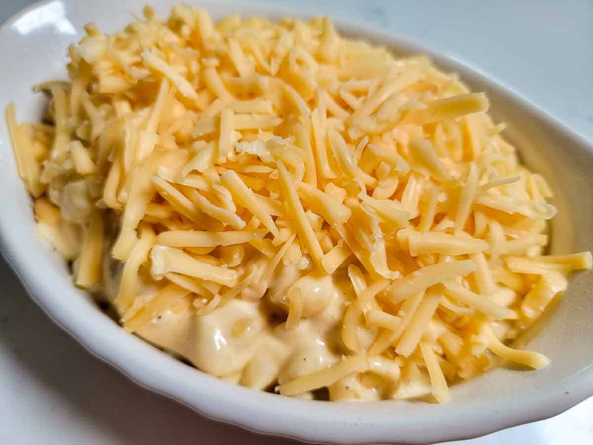 shredded cheese sprinkled onto macaroni and cheese in a baking dish.