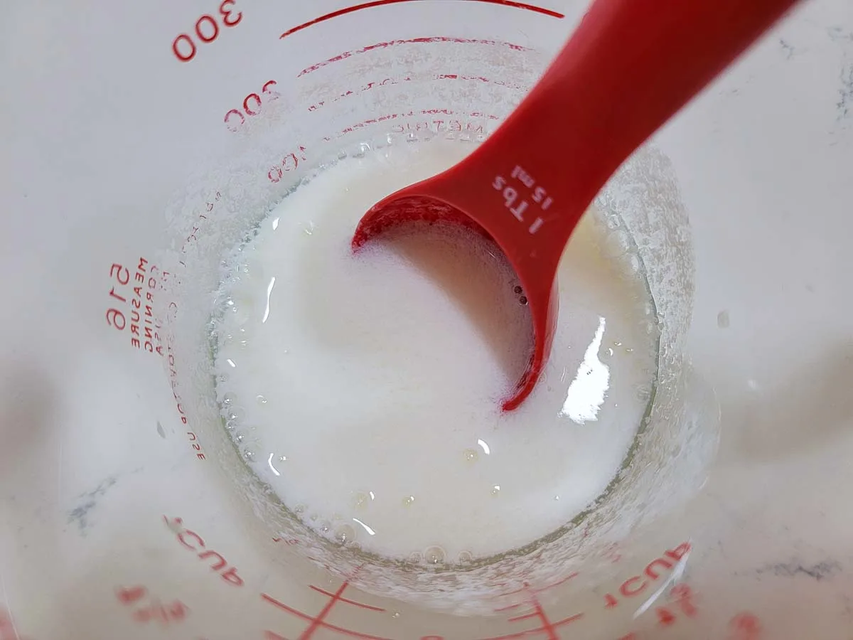 homemade buttermilk in a measuring cup with a measuring spoon.