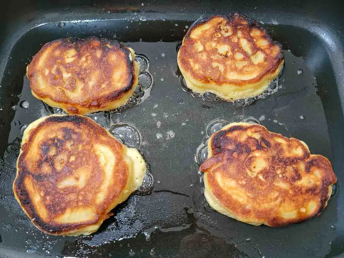 4 banana pancakes cooking in an electric skillet.
