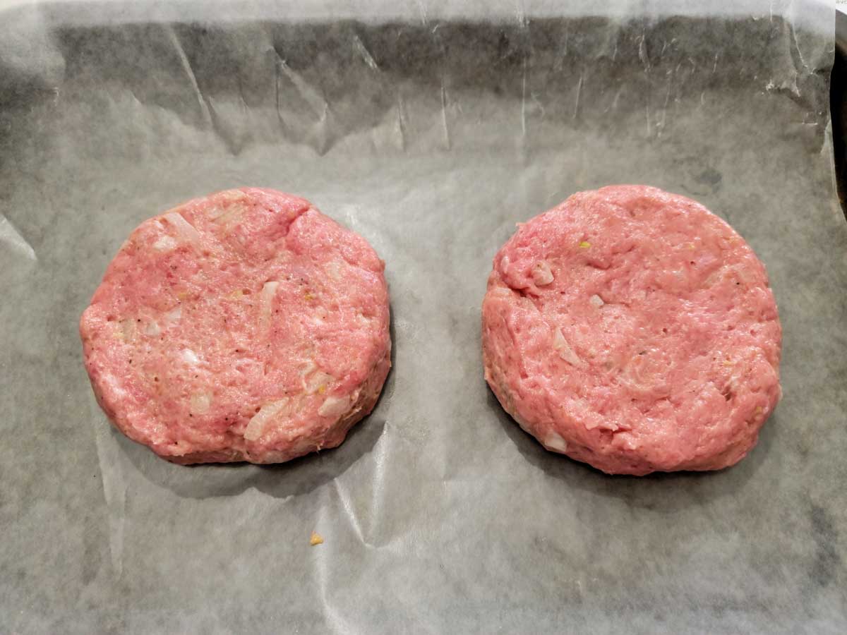 two raw turkey patties on wax paper.