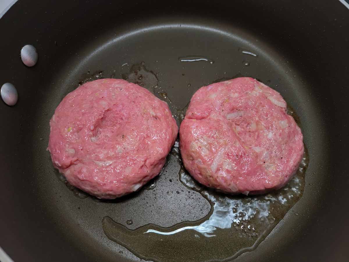 two turkey patties frying in a pan.