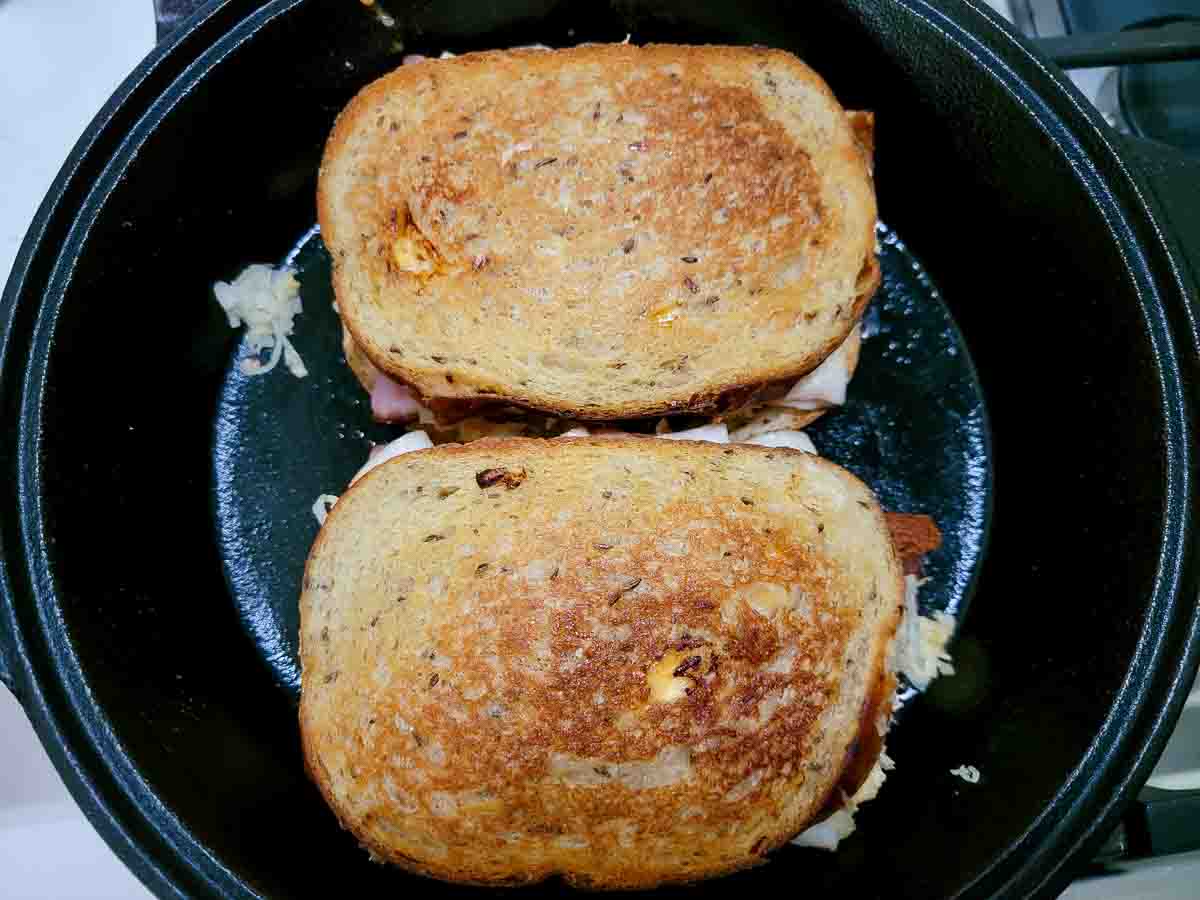 Reuben sandwich with ham cooking in a cast iron skillet.