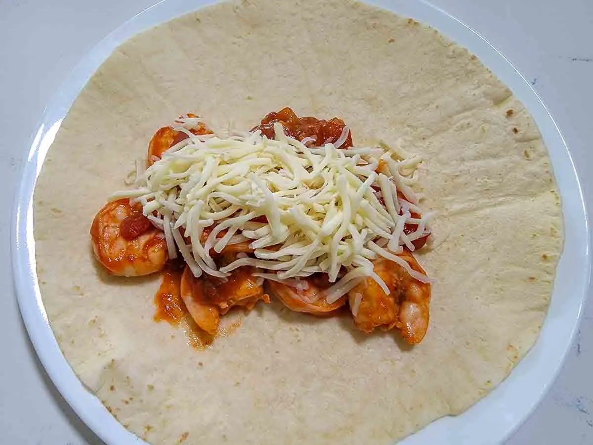 white shredded cheese on top of shrimp mixture on a large tortilla.