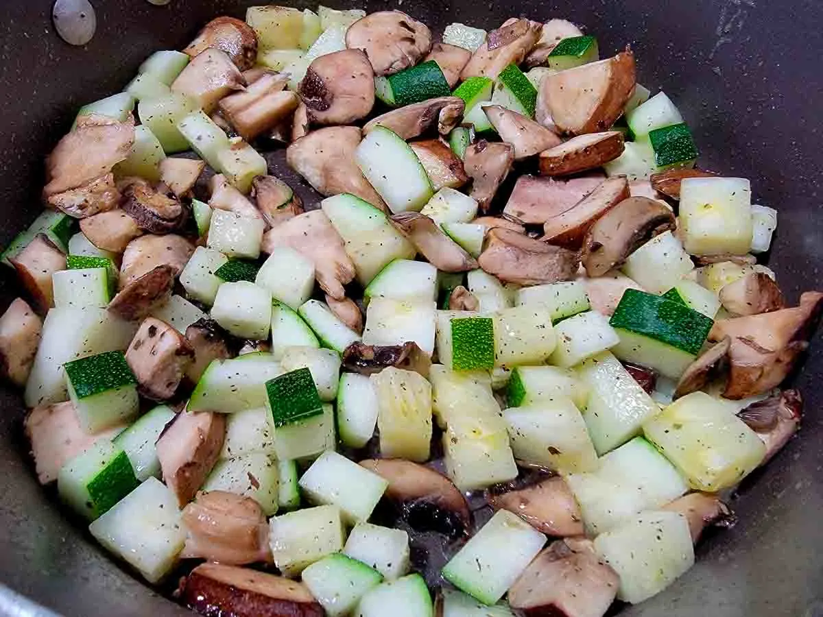 zucchini and mushrooms cooking in a pan.