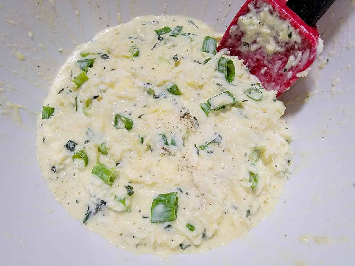 cheese, sour cream, green onions, beaten egg, basil, salt, and black pepper mixed in a bowl.
