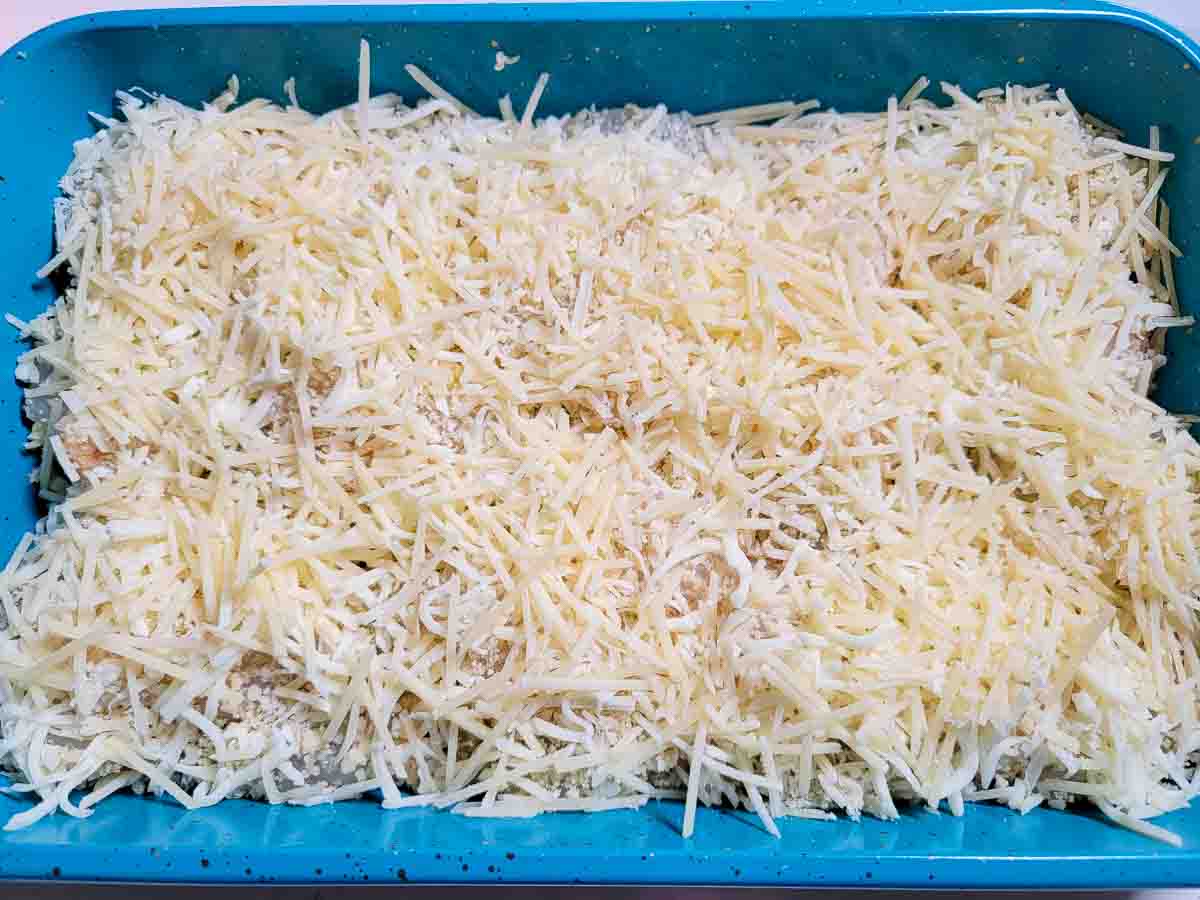 mozzarella and parmesan sprinkled over scallops and shrimp in a baking dish.