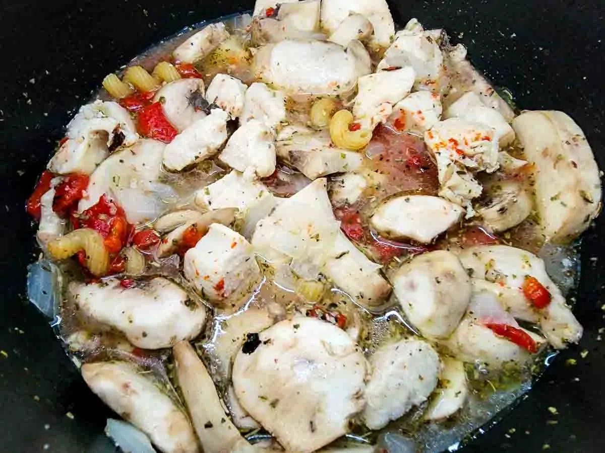 chicken broth, garlic, mushrooms, pasta, Italian seasoning, roasted red peppers, salt, and pepper added to chicken cooking in a pan.