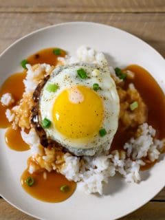Loco Moco Plate with white rice topped with a beef patty, topped with brown gravy, topped with an egg on a plate.