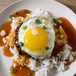 Loco Moco Plate with white rice topped with a beef patty, topped with brown gravy, topped with an egg on a plate.