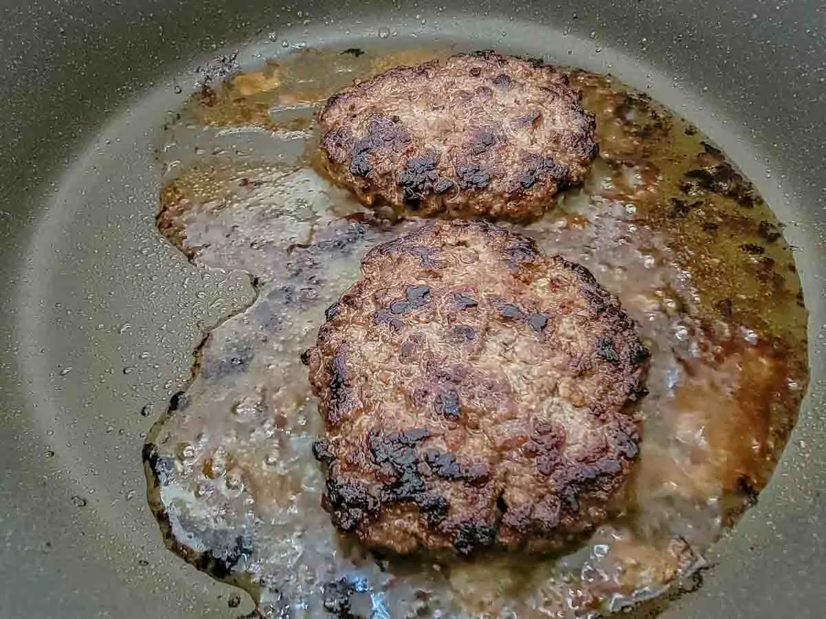 two beef patties cooking in a skillet.