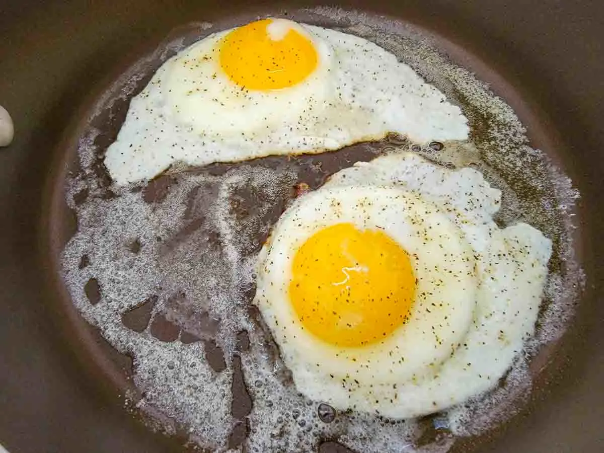 two sunny side up eggs cooking in a skillet.