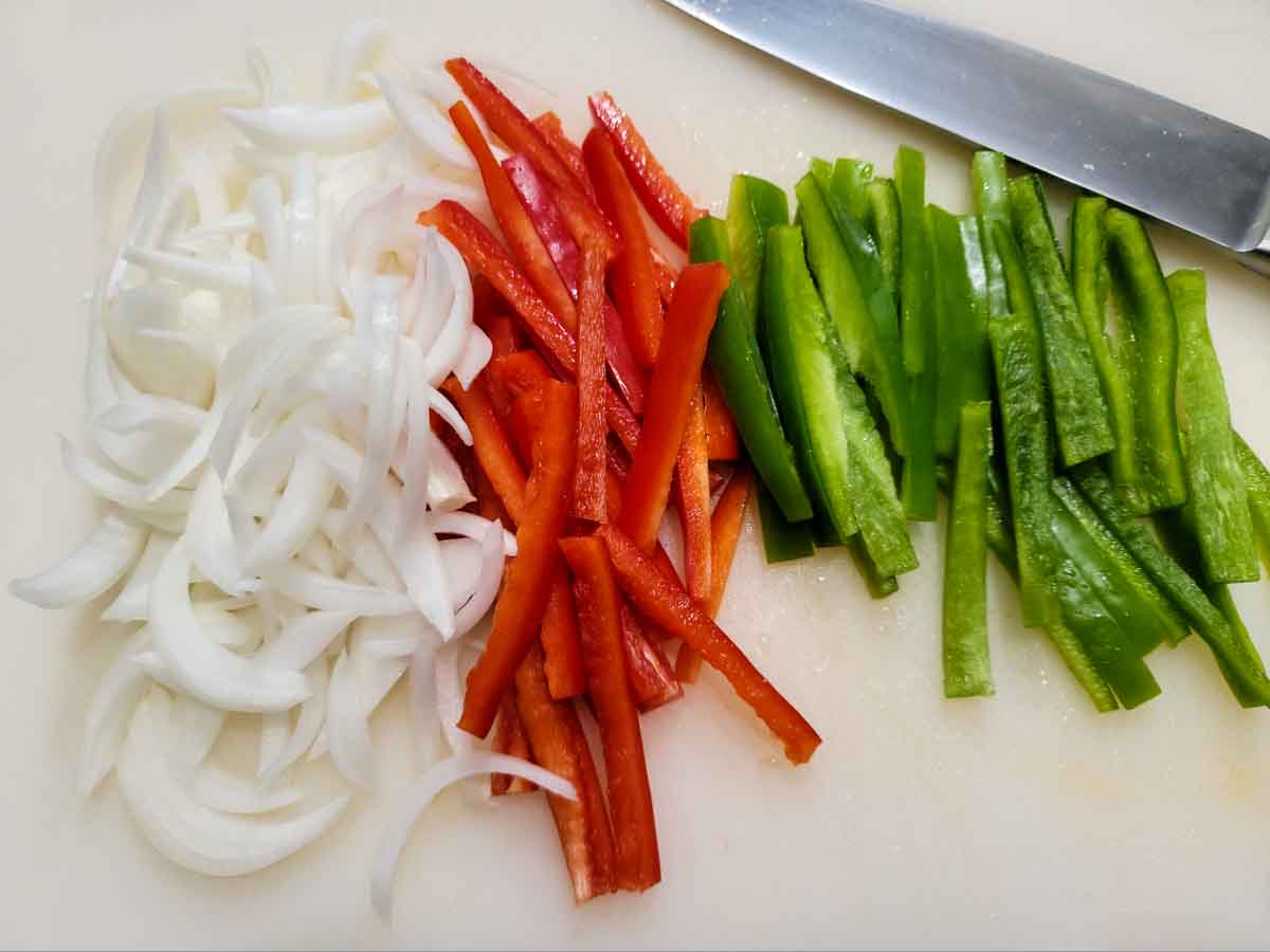 sliced green peppers, red peppers, and onions on a cutting board.