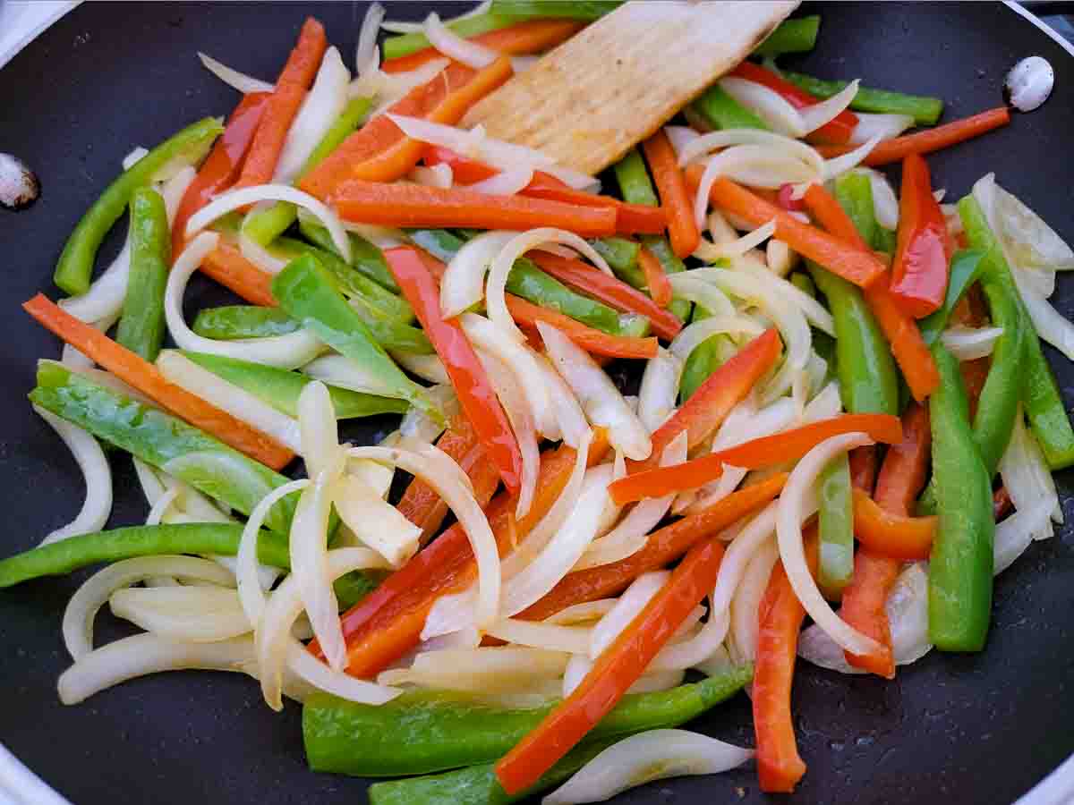 sliced red pepper, green pepper, and onion cooking in a skillet.